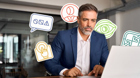 man with beard staring at computer with graphic icons around him