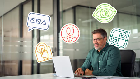 man with beard and glasses, smiling at computer with graphic icons around him 